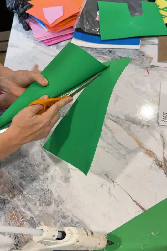 Cutting green foam sheet with scissors to shape a pointed hat for a DIY kids gnome costume.