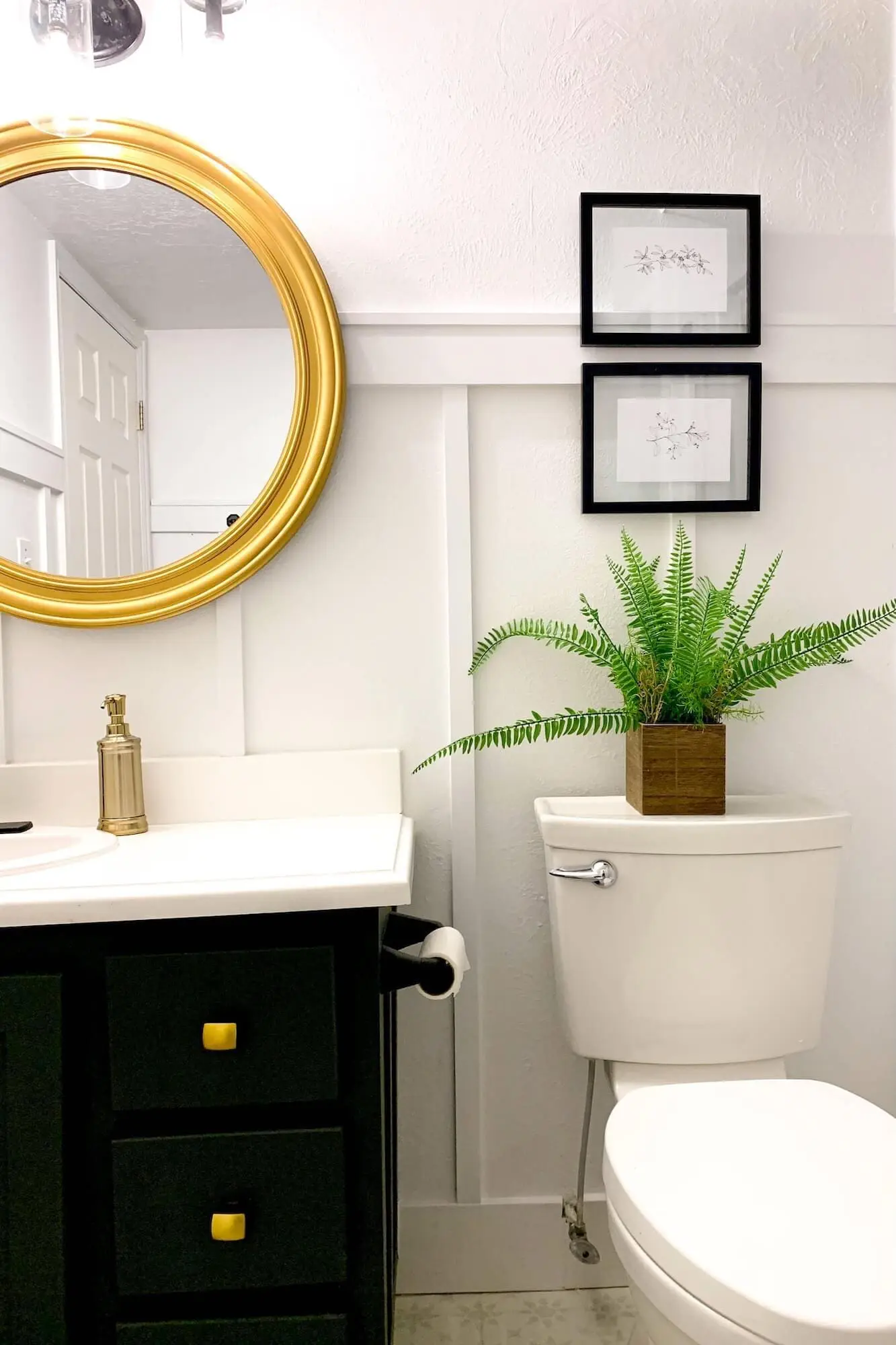 Finished board and batten bathroom wall around the vanity with a round gold mirror, black faucet, and dark green cabinet.