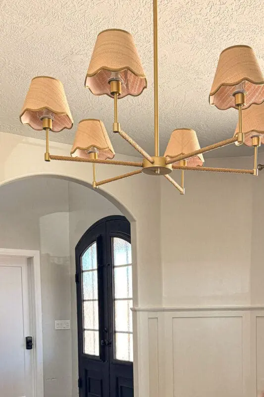 Close-up of brass chandelier with scalloped fabric shades in a formal living room with Accessible Beige walls, board and batten, arched doorway, and black double doors.