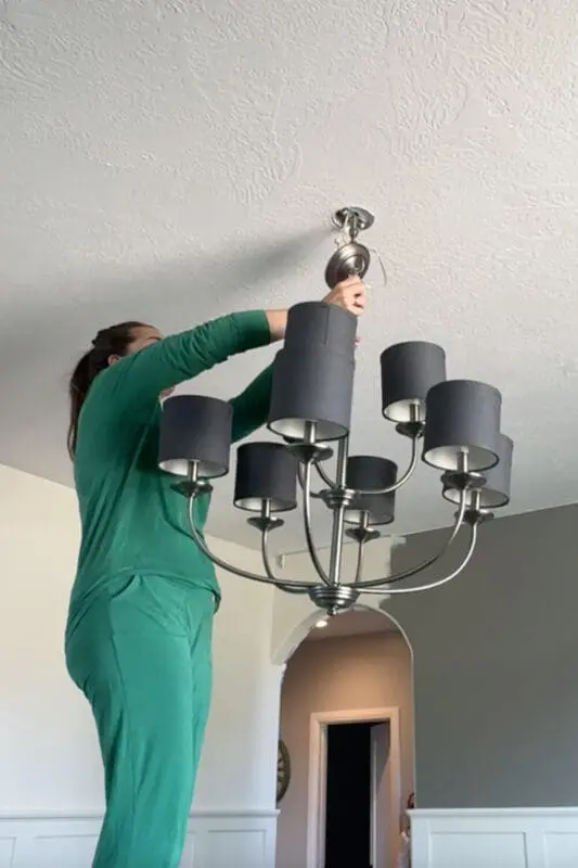 Removing the old brushed-nickel chandelier with dark drum shades during a quick makeover, board and batten walls and gray paint visible.