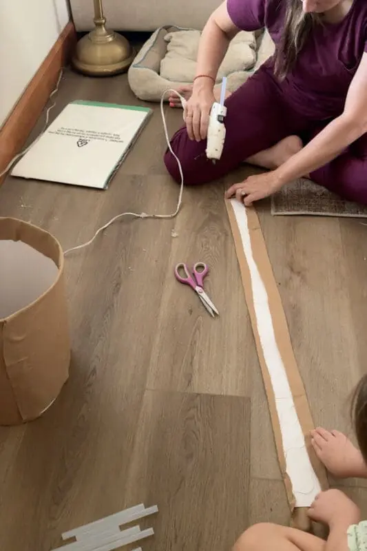 Gluing a long brown fabric strip to poster board to make the rolled rim band for the terra cotta pot skirt in a no sew DIY Halloween outfit.