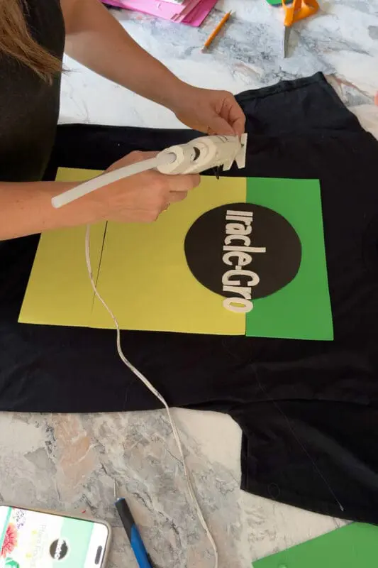 Close-up of gluing white foam letters onto a colorful DIY costume t-shirt design, a simple and funny Halloween shirt idea made with craft supplies.