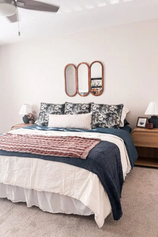 guest room refresh with cozy fall bedding, navy quilt layered over cream duvet, rust knit throw, patterned euro pillows, gingham lumbar, wood nightstands, triple wood mirror