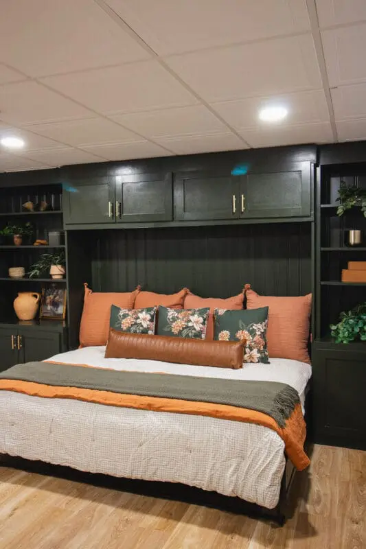 horizontal murphy bed pulled down with fall bedding, green built-ins and styled shelves in basement guest room