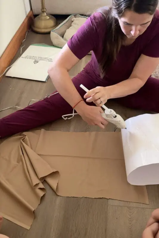 Applying hot glue to a white poster-board cylinder before wrapping it with brown fabric to make the a fabric, wearable planter pot for Halloween.
