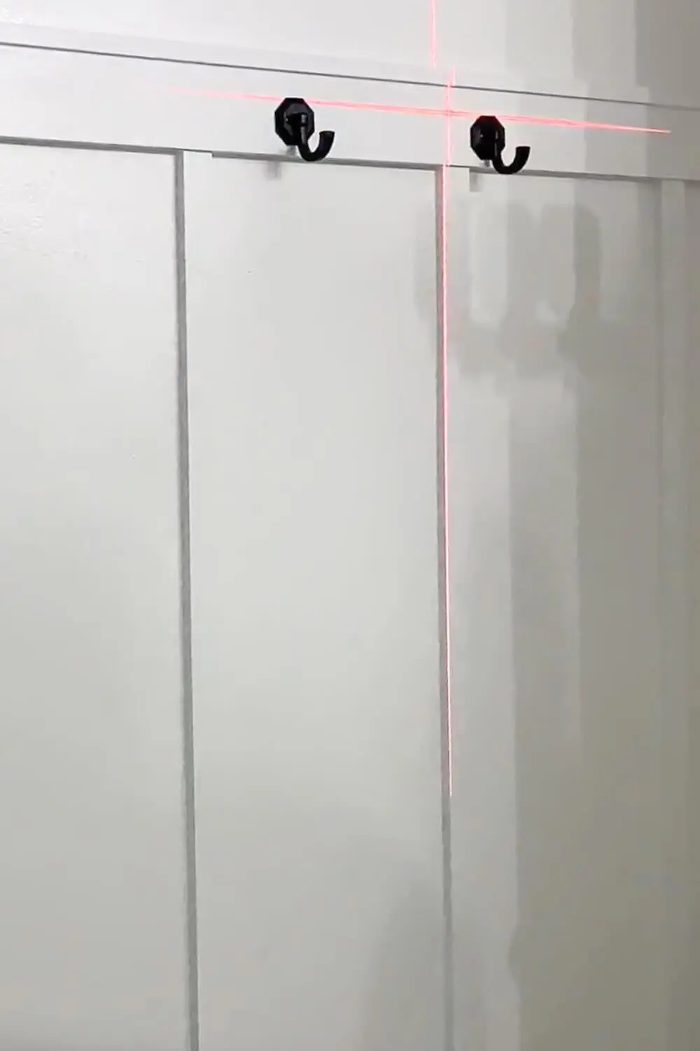 White board and batten bathroom wall with black hooks along the top rail, laser line aligning the hardware.