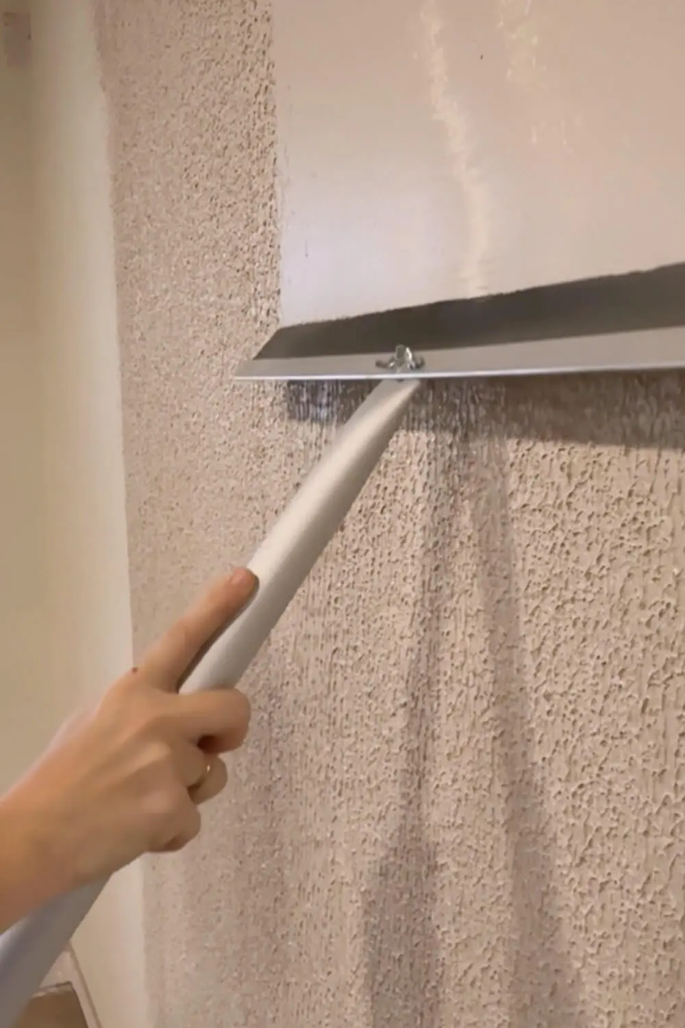 Pulling a wide drywall trowel over rolled-on joint compound to skim coat a textured wall and knock down the texture