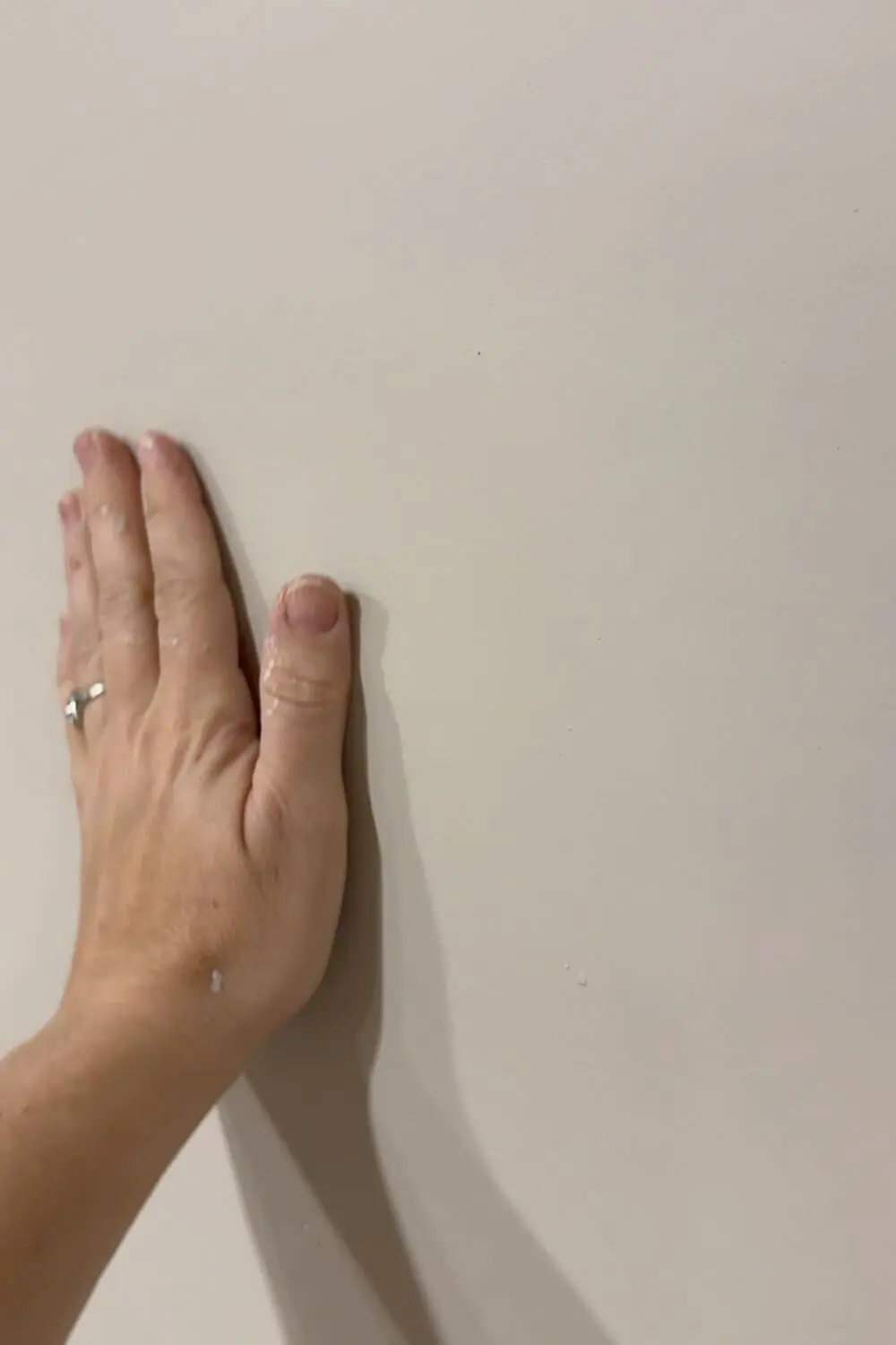 After skim coating a wall, a hand touches the smooth, finished surface with no visible texture.