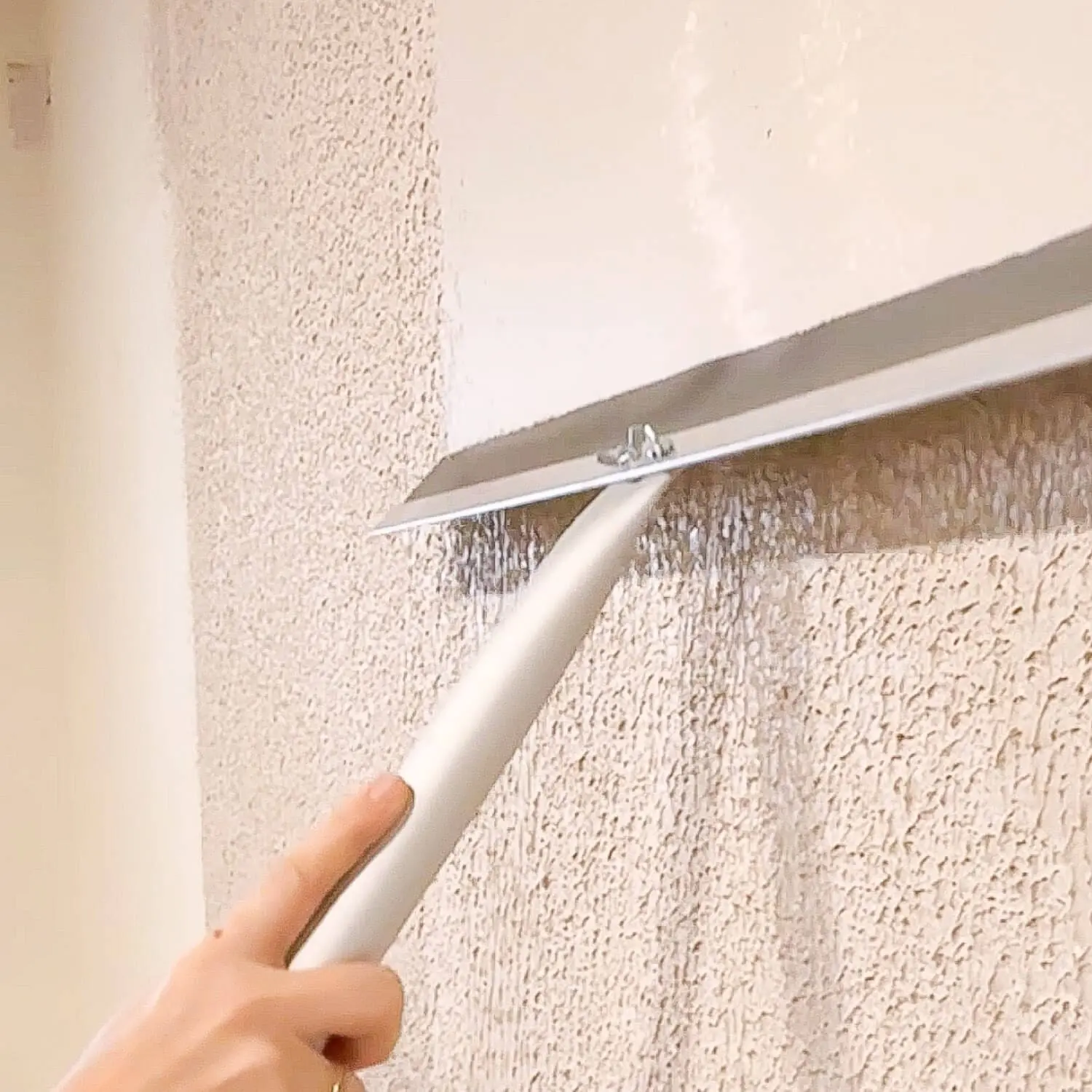 Using a wide drywall trowel to skim coat over heavy wall texture, flattening the surface as the joint compound is pulled smooth