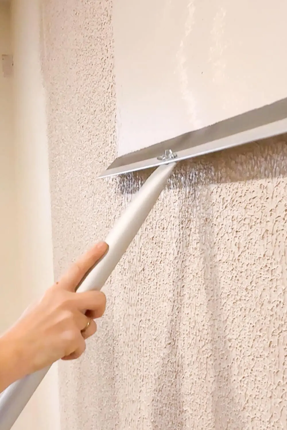 Pulling a wide drywall trowel across rolled-on joint compound to knock down textured drywall and start creating a smooth wall finish