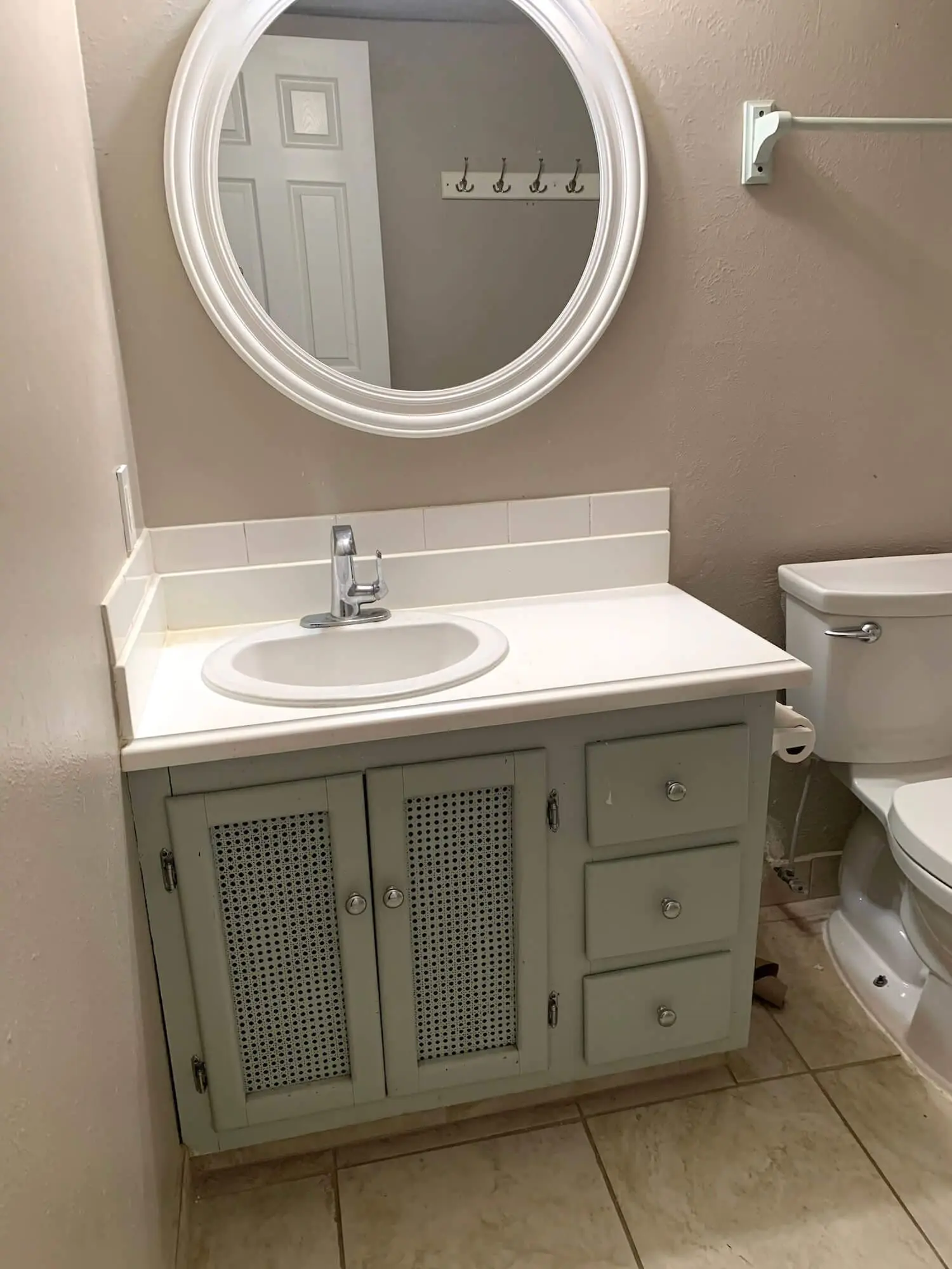 Before photo of the bathroom vanity and round mirror with beige walls and outdated finishes.