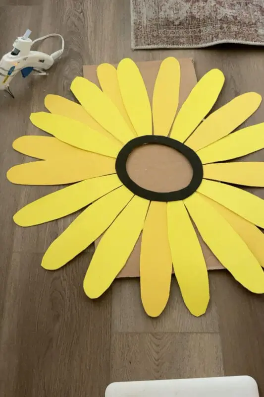 Sunflower headpiece layout with long yellow cardstock petals and a black face ring on a cardboard base, ready to glue for an easy no sew flower costume.