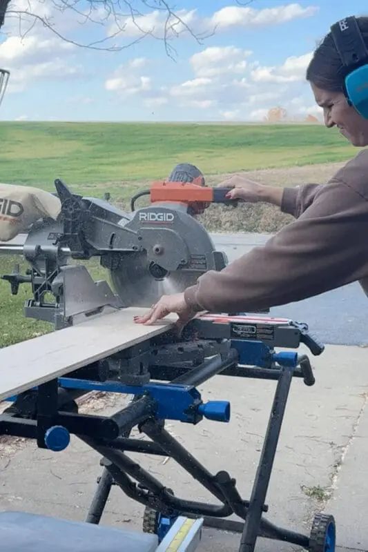 Woman using a miter saw to cut narrow plywood strips for a custom kitchen cabinet cookware organizer.
