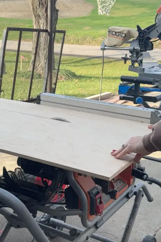 Cutting a large sheet of plywood on a table saw outside to build a DIY kitchen drawer organizer.
