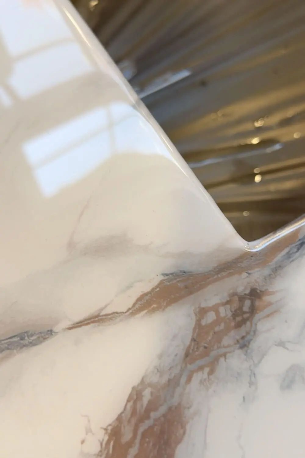 Detail of smooth epoxy edge on DIY marble-look countertops, highlighting the seamless transition from faux marble contact paper into the undermount stainless steel kitchen sink.