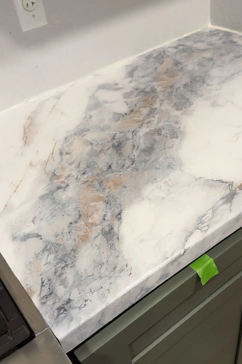 DIY countertops that look like marble in a small kitchen, showing the marble contact paper pattern sealed with epoxy above green cabinets.