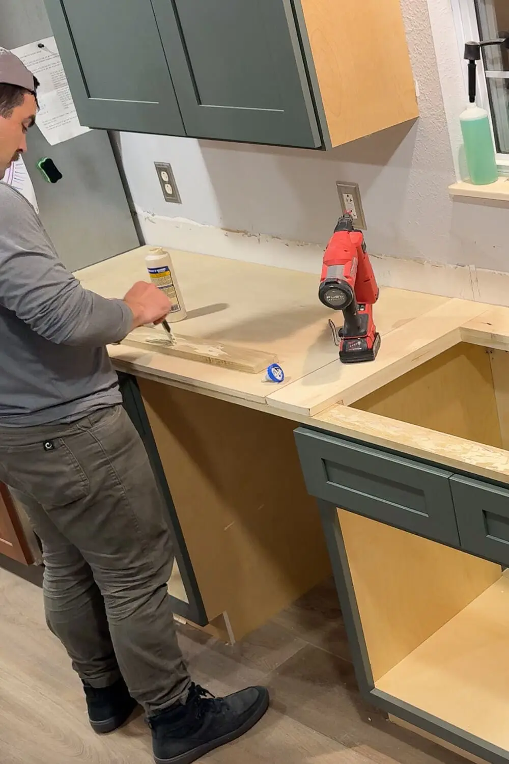 Spreading wood glue on a trim board while building plywood counters, prepping the area for a kitchen sink.