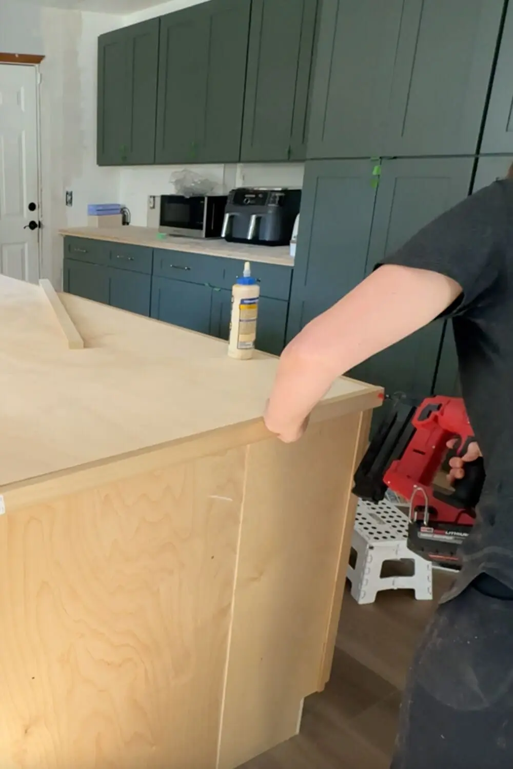 Pressing the front edge trim onto a plywood kitchen island counter, step in building budget-friendly counters that will be wrapped in faux marble and sealed with epoxy.