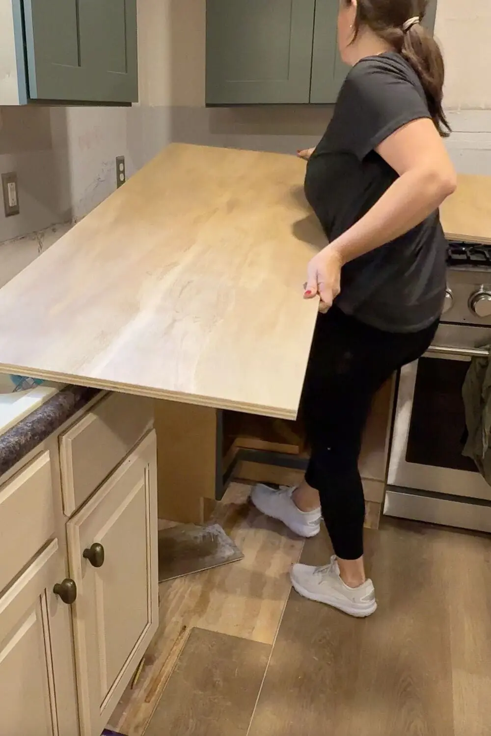 Lifting a large sheet of plywood onto kitchen cabinets while installing DIY countertops, showing the raw plywood base before the faux marble and epoxy finish.