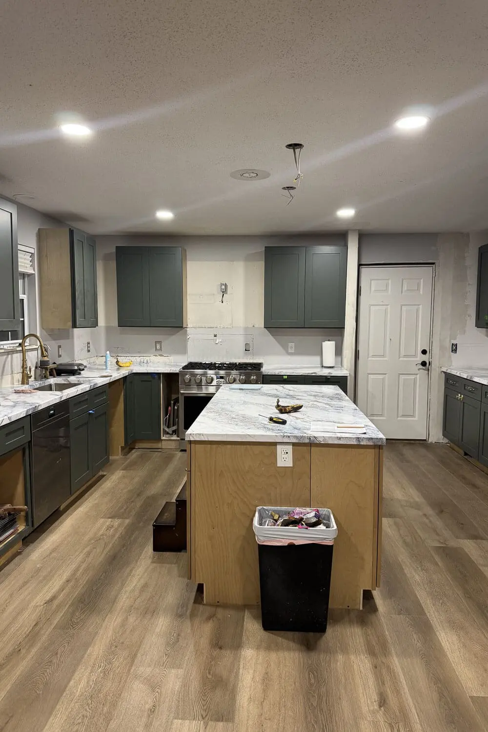 Work-in-progress kitchen with green shaker cabinets and DIY countertops that look like marble, featuring a large plywood island wrapped in faux marble epoxy counters.