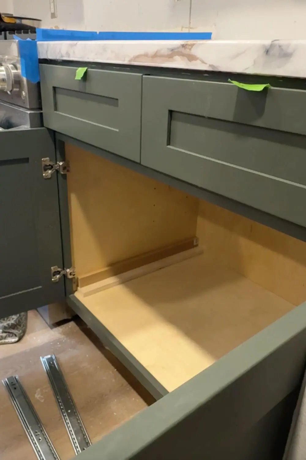 Empty lower kitchen cabinet with green doors and faux marble countertop, prepped for a DIY kitchen organization project.