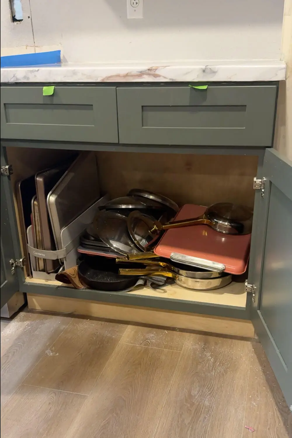 Cluttered lower kitchen cabinet crammed with stacked pots, pans, lids, and baking sheets showing the messy before photo before adding organized pots and pans storage.