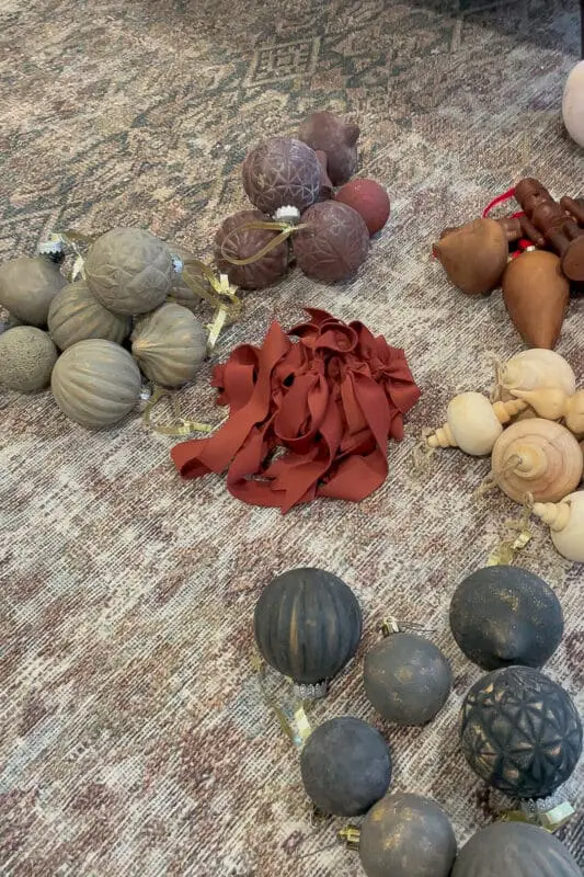 Neutral and black textured Christmas ornaments with satin ribbon laid out on a patterned rug, ready to be finished with Rub n Buff.