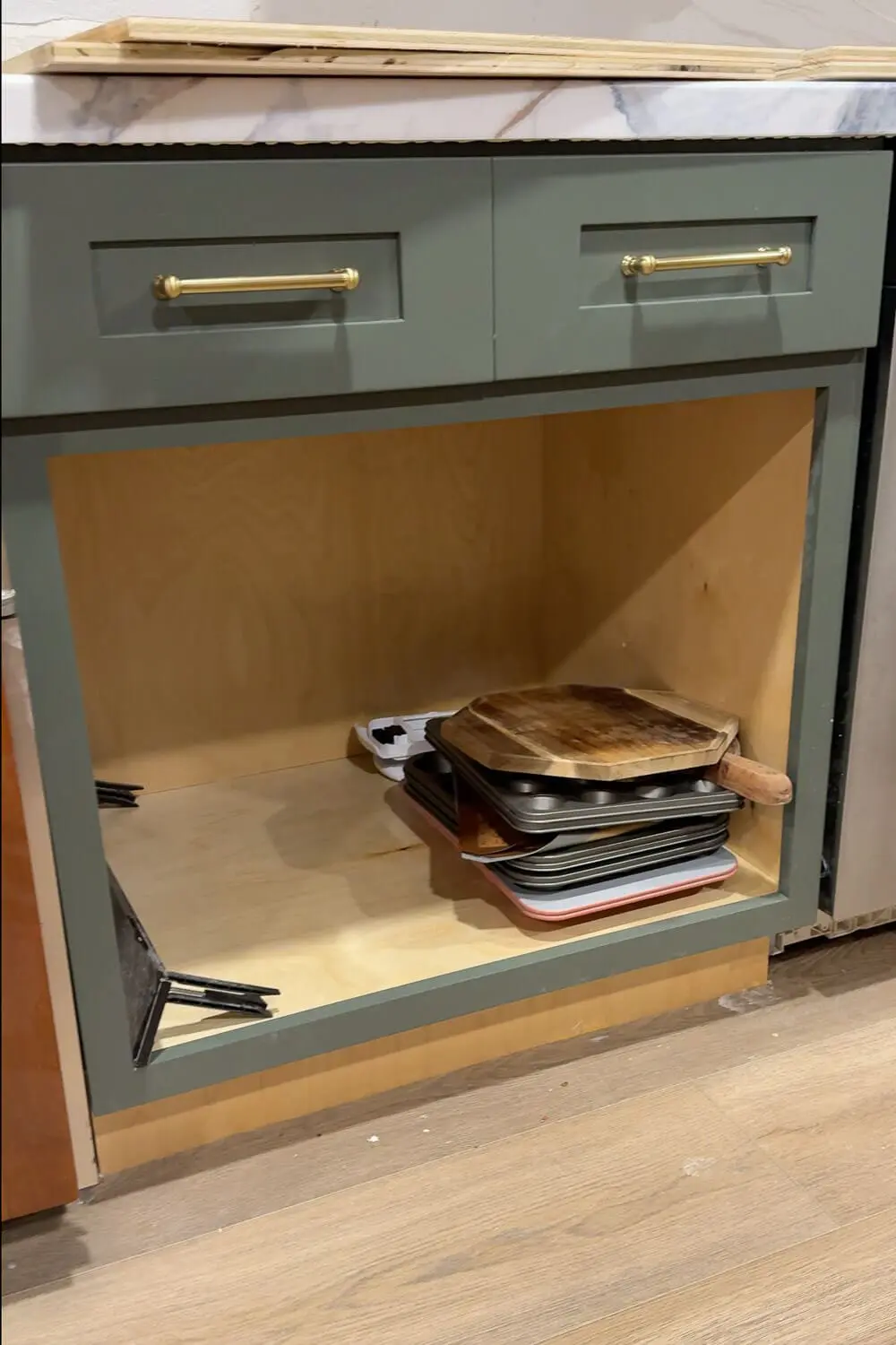 Deep lower kitchen cabinet with baking sheets and cutting boards stacked in a messy pile before adding a DIY sheet pan organizer