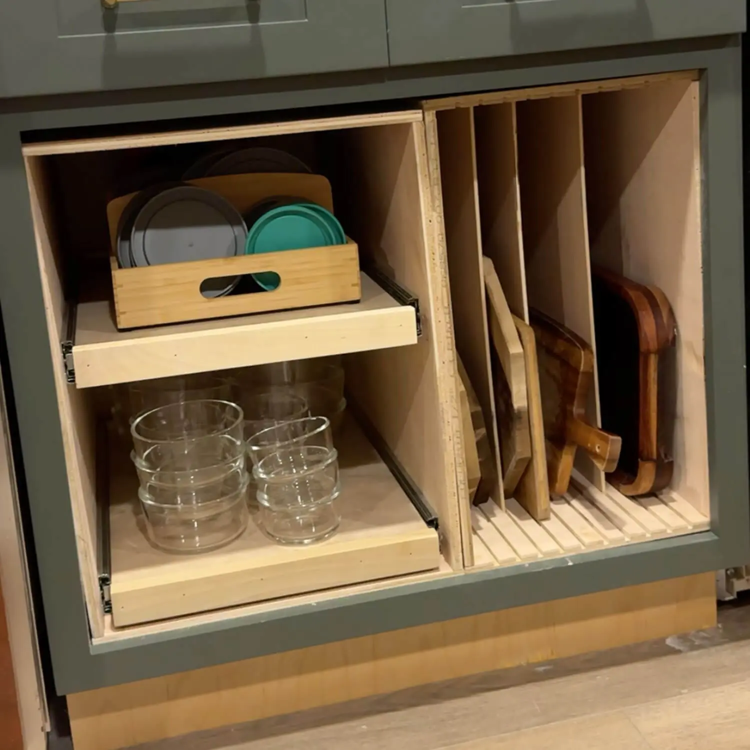 DIY sheet pan organizer in a lower kitchen cabinet with vertical plywood dividers holding cutting boards and pull out storage for glass containers