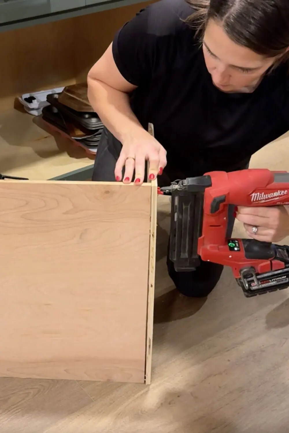 Using a brad nailer to attach the side panel to the plywood box for a custom DIY sheet pan organizer cabinet insert