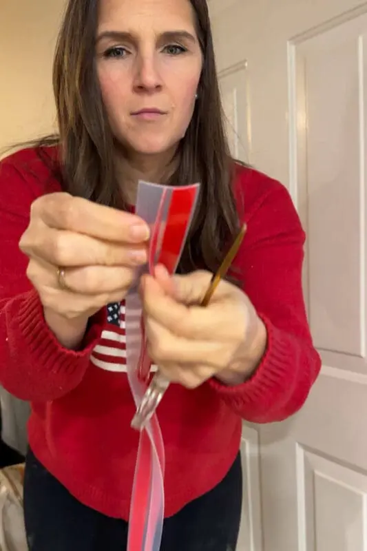 DIY blogger peeling the red adhesive backing from a clear weatherstripping strip for a front door