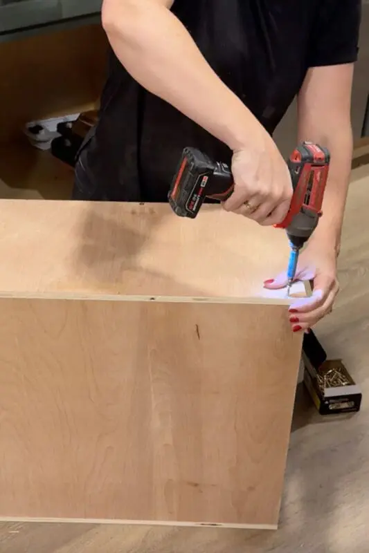 Driving screws into the corner of a plywood box to build a sturdy DIY vertical storage cabinet insert