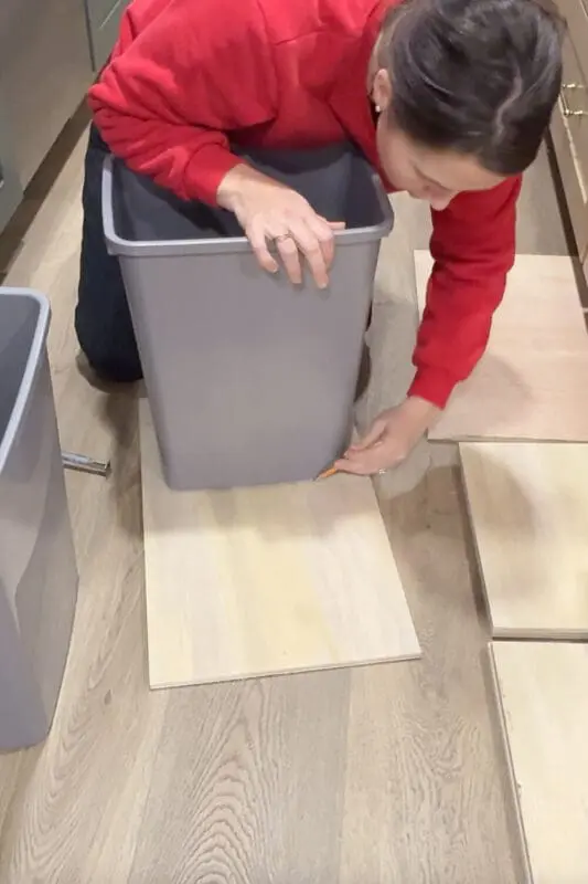 Marking the outline of a gray trash can on a plywood board to plan the layout for a custom DIY double trash can cabinet drawer.