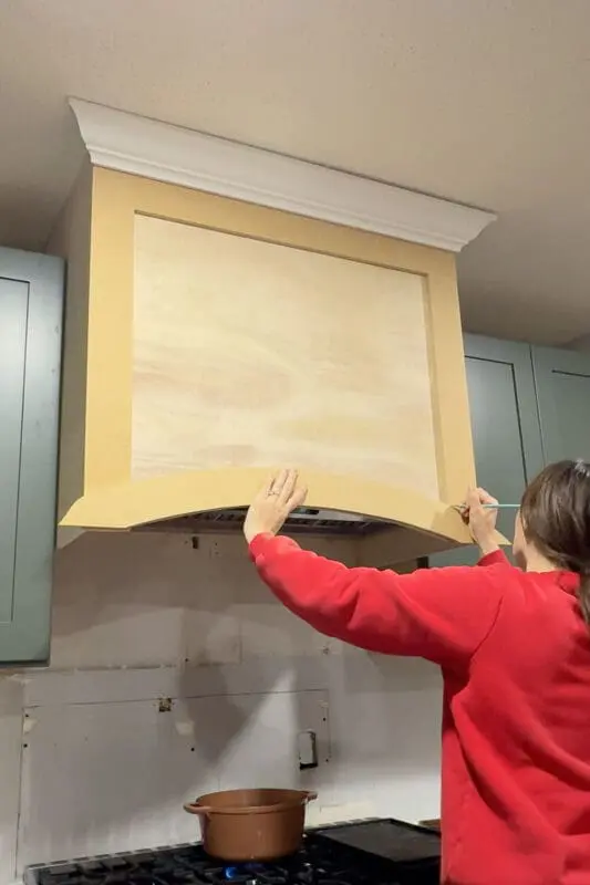 I hold the arched trim in place and mark the edges for a precise fit on the front of the custom range hood cover.
