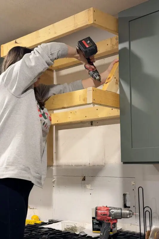 Attaching an angled 2x4 support brace to connect the top and bottom of the DIY range hood cover frame.
