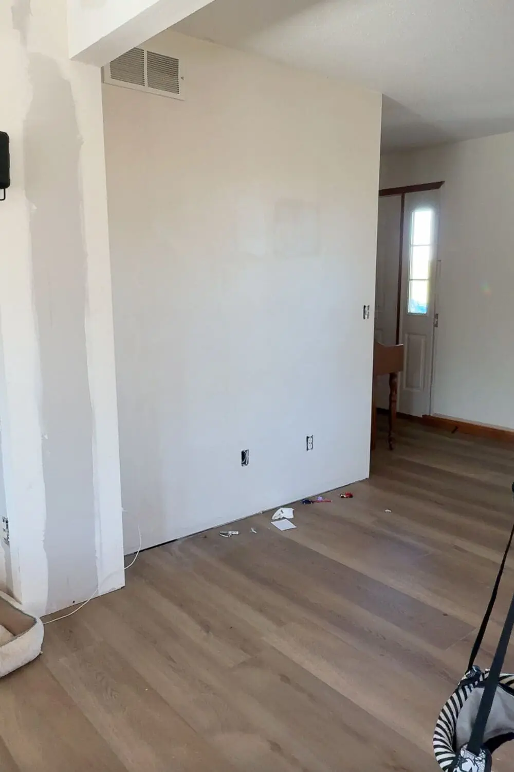 Before photo of a plain white wall with a floor vent and electrical outlets, prepped and ready for a DIY wall trim upgrade.