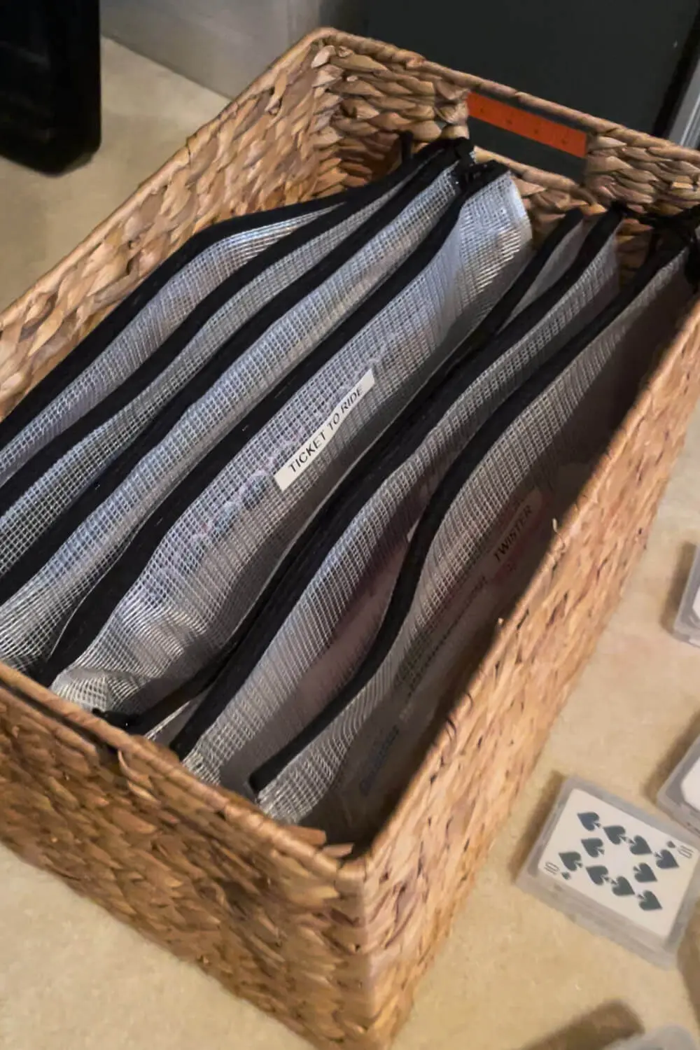 Board Game Storage Ideas with a woven basket filled with labeled mesh zipper bags for board games, keeping game boards and pieces organized, vertical, and easy to grab.