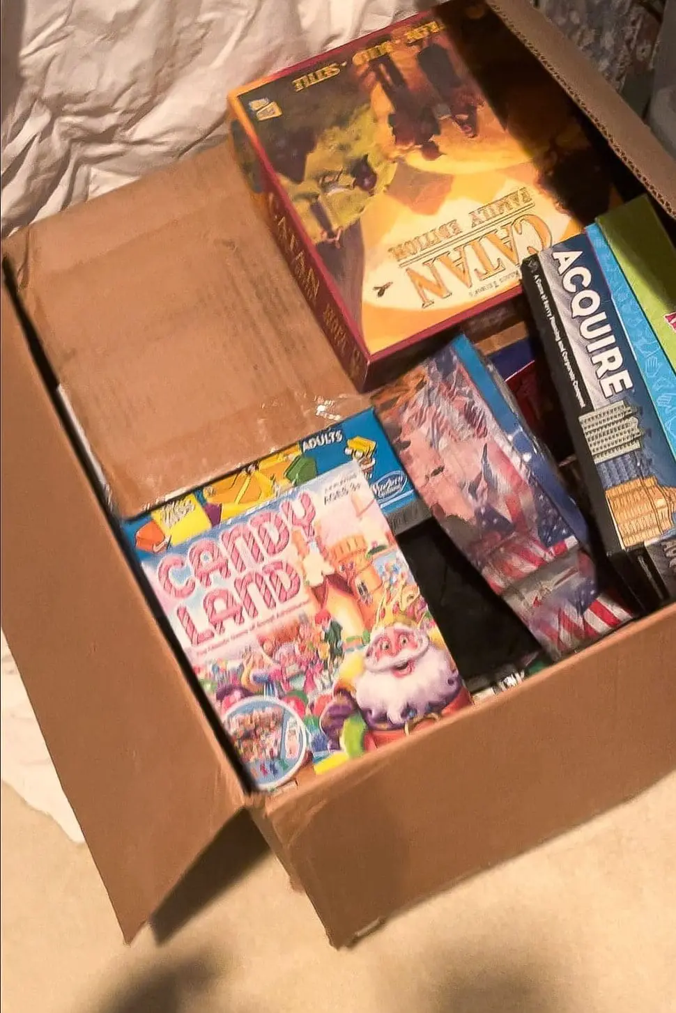 Board Game Storage Ideas starting with a declutter, showing a cardboard box filled with board games and card games pulled from a closet before reorganizing into stackable containers.
