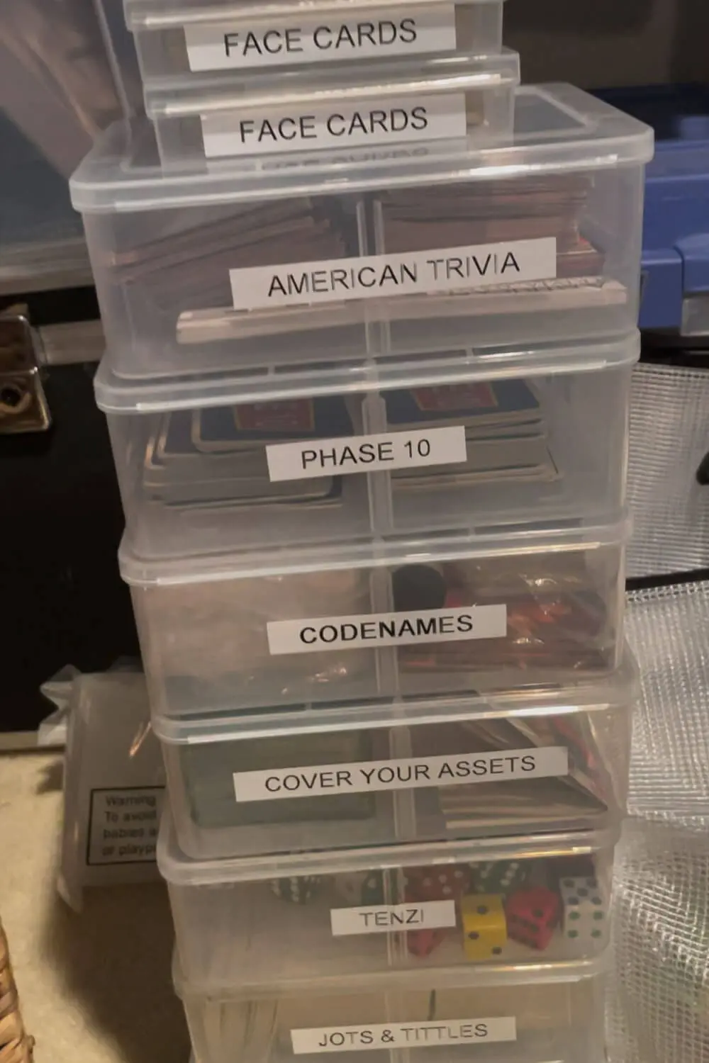 Stack of plastic cases labeled for card games and dice games, making it easy to store and grab favorites like Phase 10, Codenames, and Tenzi.