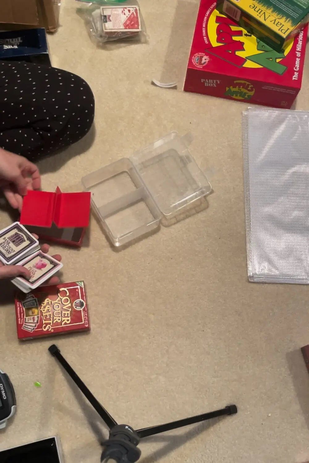 Board Game Storage Ideas in progress, sorting card game decks and pieces on the floor with plastic cases, zip bags, and a label maker to replace bulky game boxes.