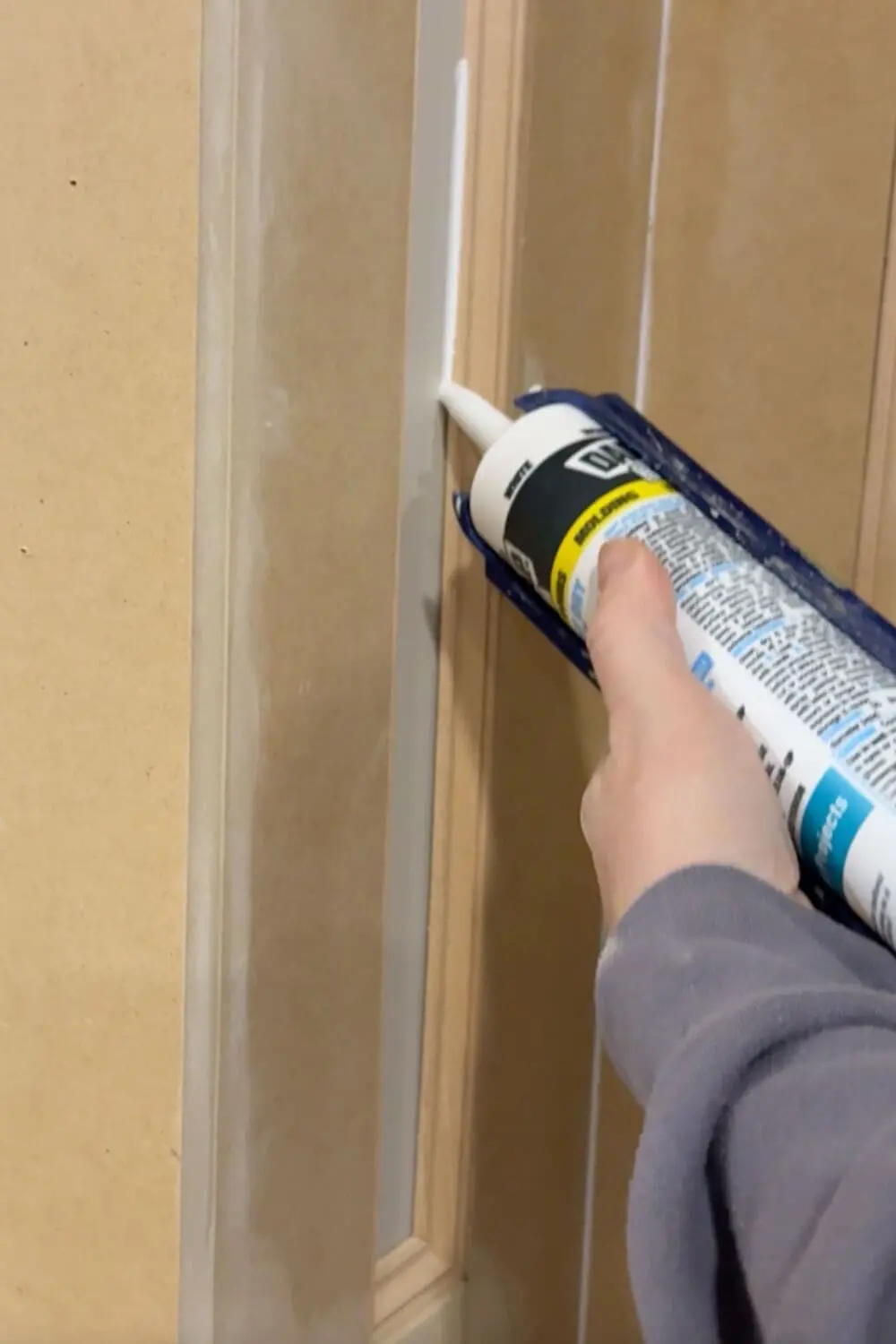 Applying paintable caulk along the inside edge of box molding wall trim to fill gaps and create clean, seamless lines before priming and painting.