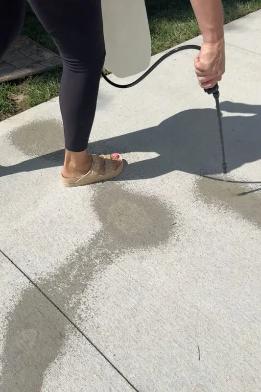 Spraying a concrete patio with a pump sprayer to treat tough, set-in stains during an outdoor concrete cleaning routine.