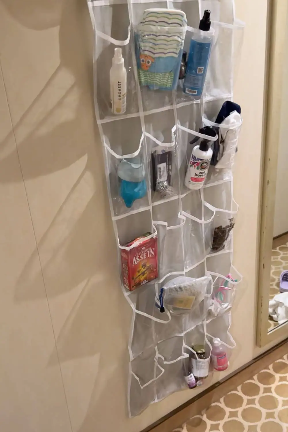 Clear hanging shoe organizer used as a cruise cabin organization hack, holding sunscreen, diapers, toiletries, kids items, and small games to keep a cruise with kids room clutter-free.