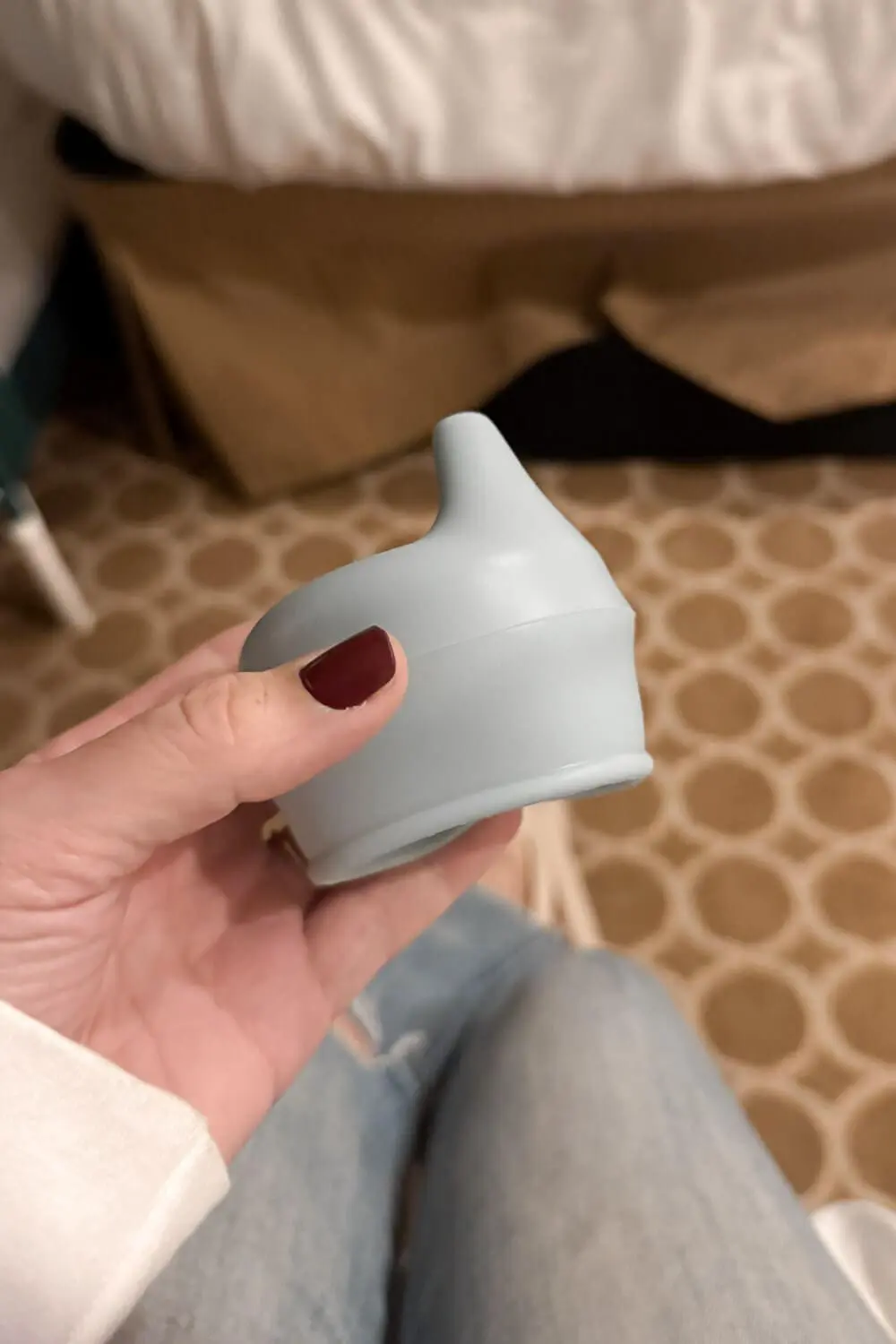 Close-up of a hand holding a silicone sippy cup lid topper inside a ship's cabin, a simple travel with children packing essential for turning regular cups into spill-resistant cups.
