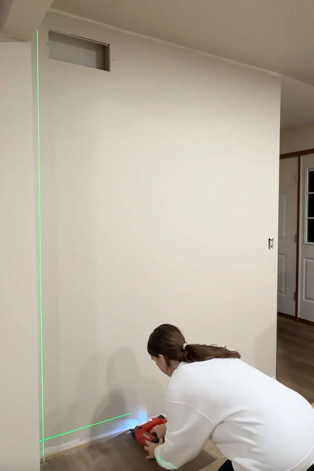 Attaching the lower trim board for DIY wall trim work with a brad nailer while lining everything up with a laser level.