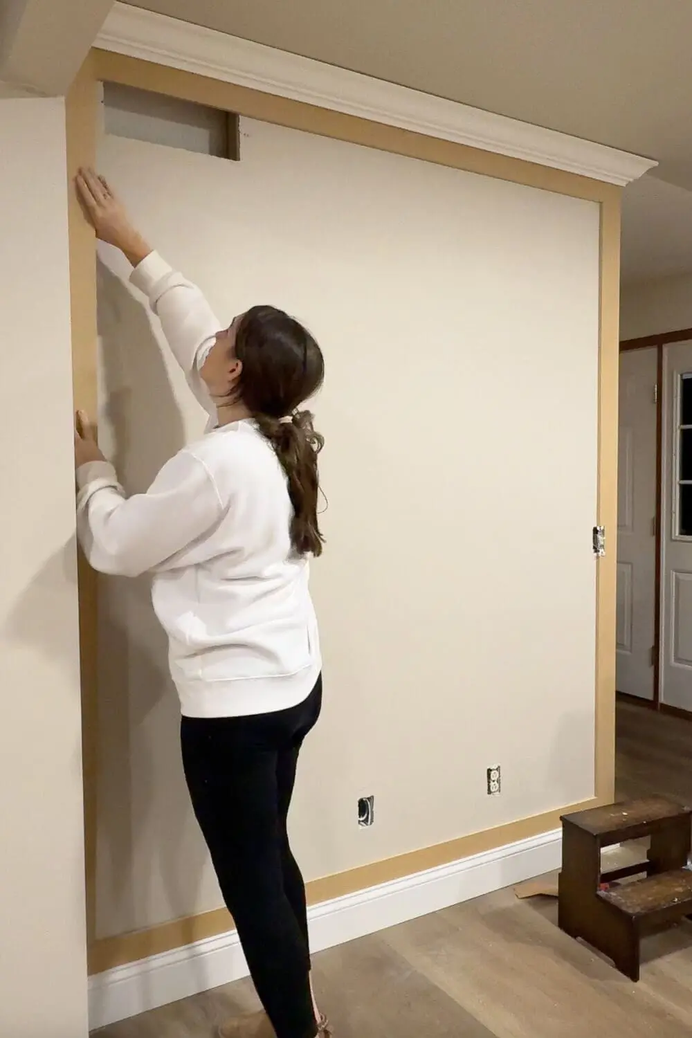 Measuring and checking spacing for the vertical boards while laying out a DIY panel wall trim design for a picture frame wainscoting look.