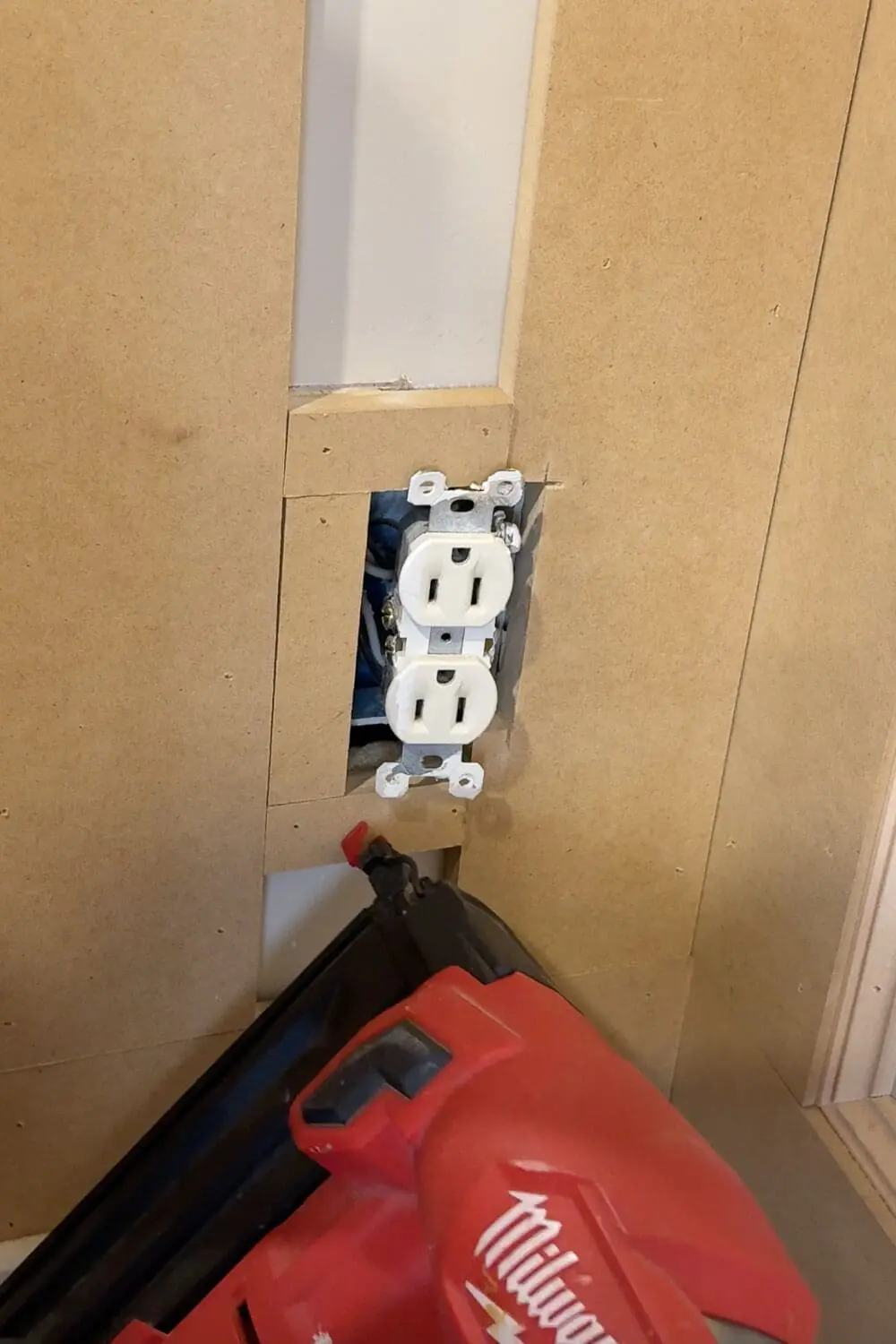 Close-up of DIY box molding wall trim cut to fit around an electrical outlet, showing how to notch trim boards before nailing.