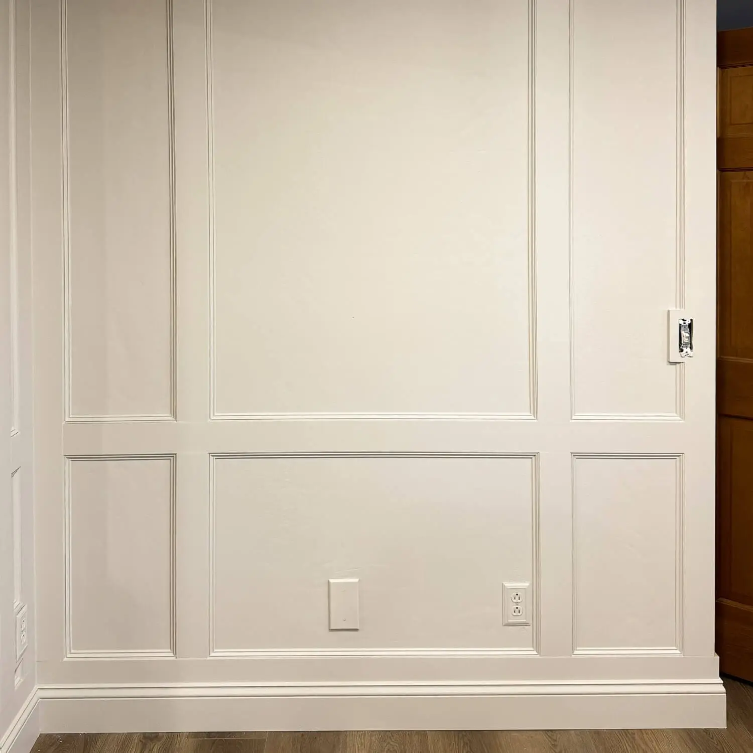 Close-up of DIY box molding wall trim showing the chair rail and lower picture frame panels around an outlet and wall plate.