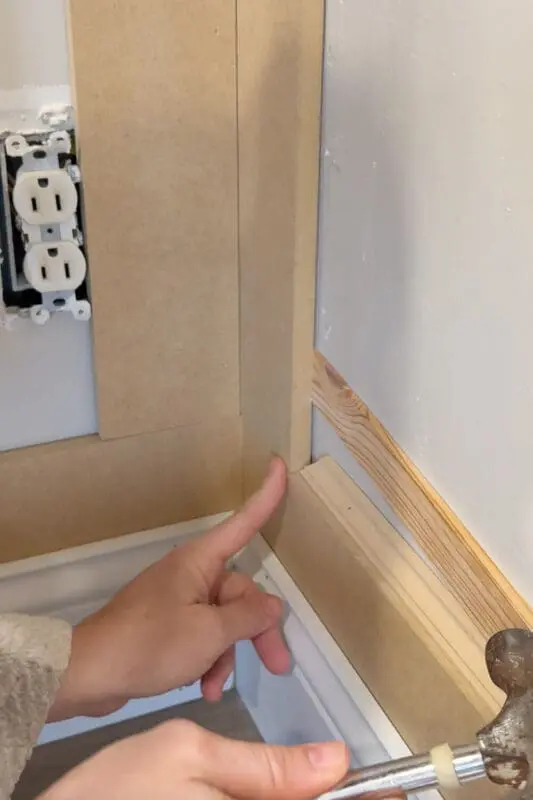 Using shims to even out wall trim on an uneven wall, showing the corner detail above the baseboard.