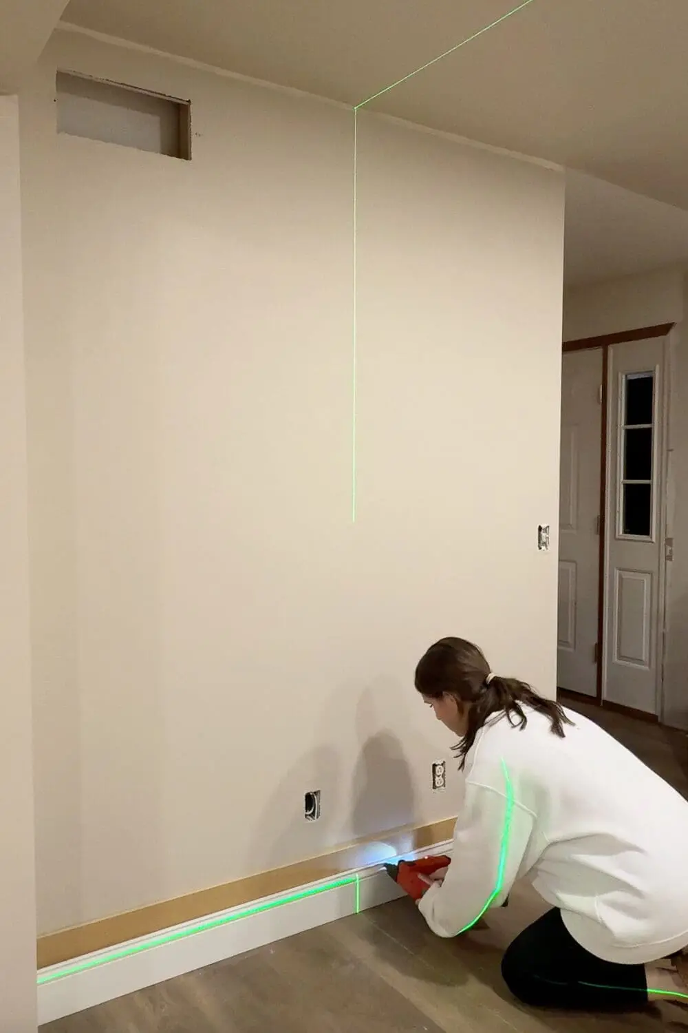 Using a green laser level to keep trim straight while attaching baseboard with a brad nailer.